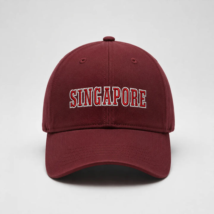 A maroon baseball cap featuring 'SINGAPORE' embroidered in arched red letters with a white outline on the front, set against a plain light gray background.