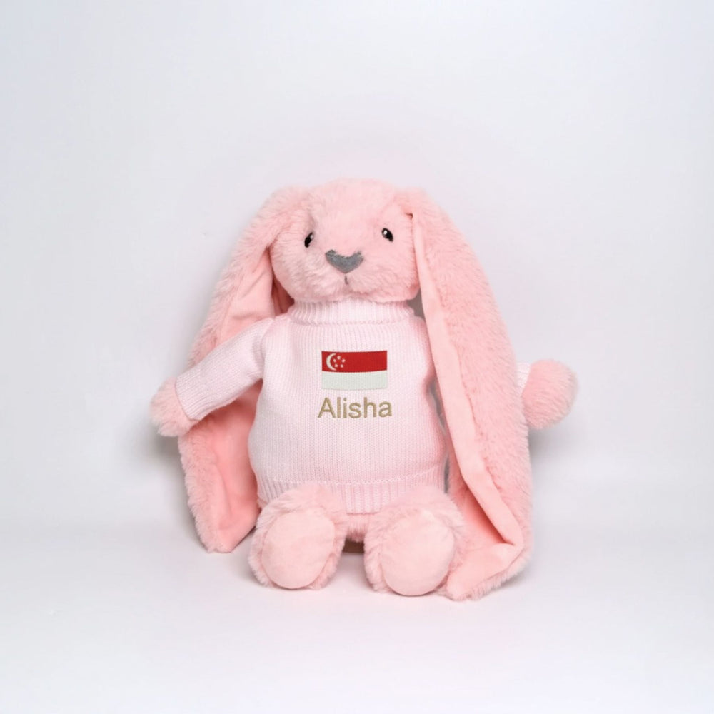 Pink plush bunny with a white shirt displaying a SG flag and name 'Alisha' on a light gray background