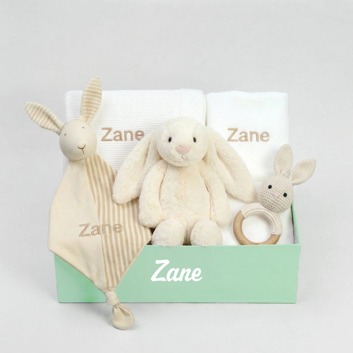 Collection of baby items including a blanket, plush toys, and a book on a light gray background.