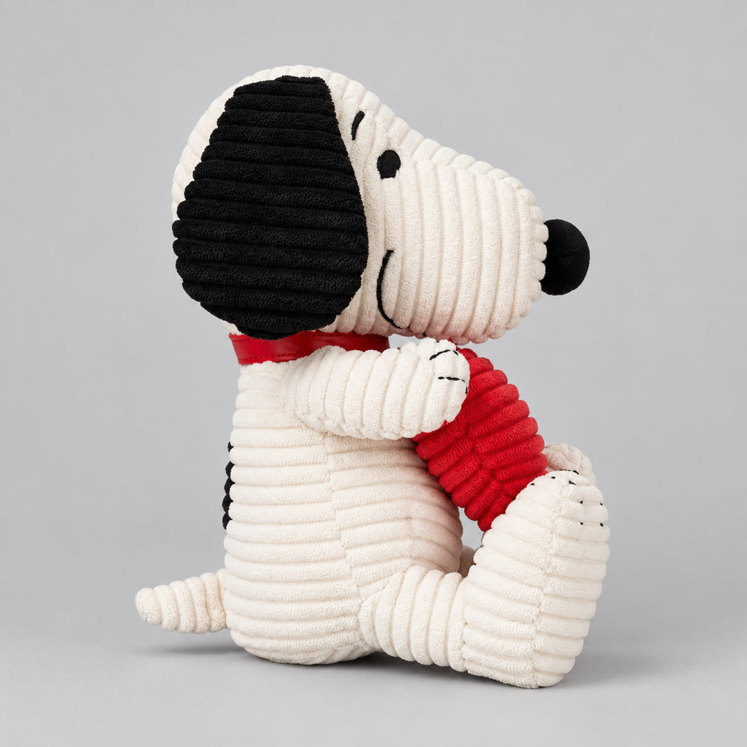 Side view of a white Snoopy plush toy with black ears, hugging a red textured heart.