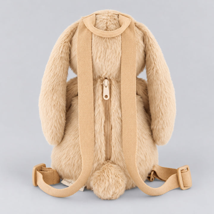 Rear view of a beige plush bunny backpack featuring adjustable woven shoulder straps, a central zippered compartment and a fluffy bunny tail.