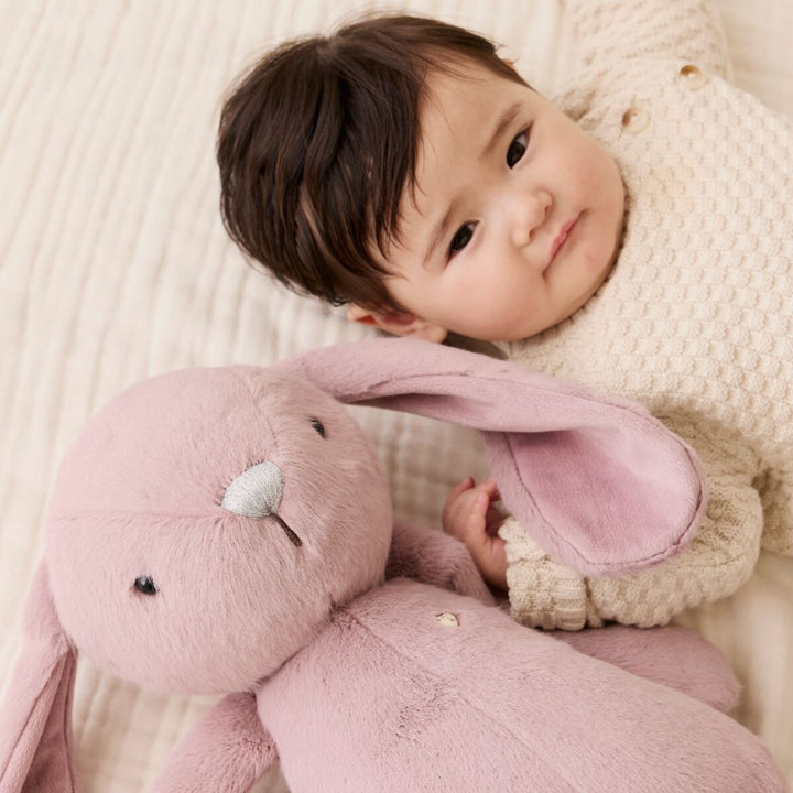 Baby lying on a cream blanket beside a soft pink Snuggle Bunnies plush bunny.