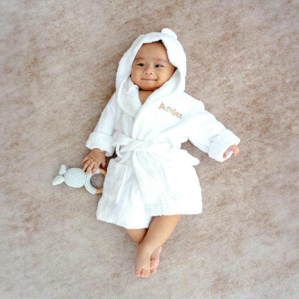 Baby in white bamboo robe with "Ander" customised in beige thread
