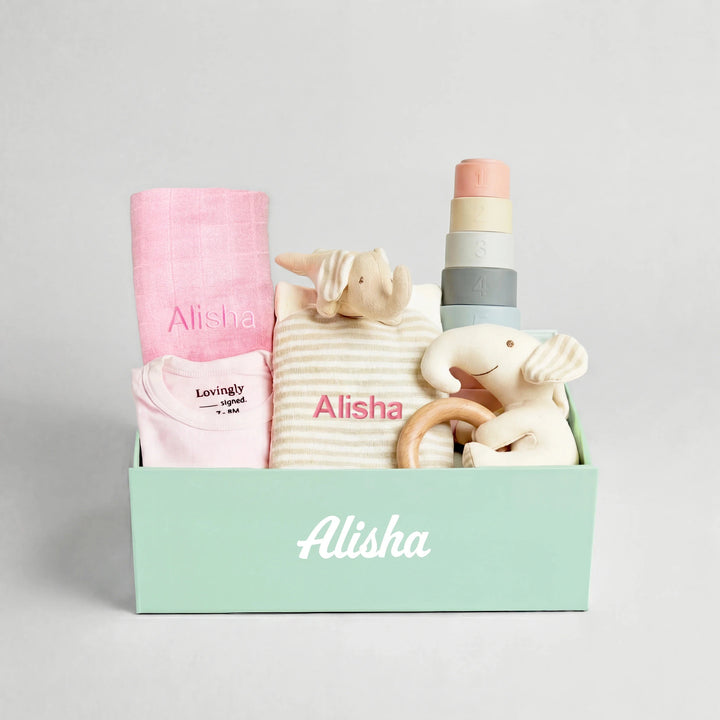 Pink Baby gift set with clothes, toys, and a blanket in a lovingly signed gift box