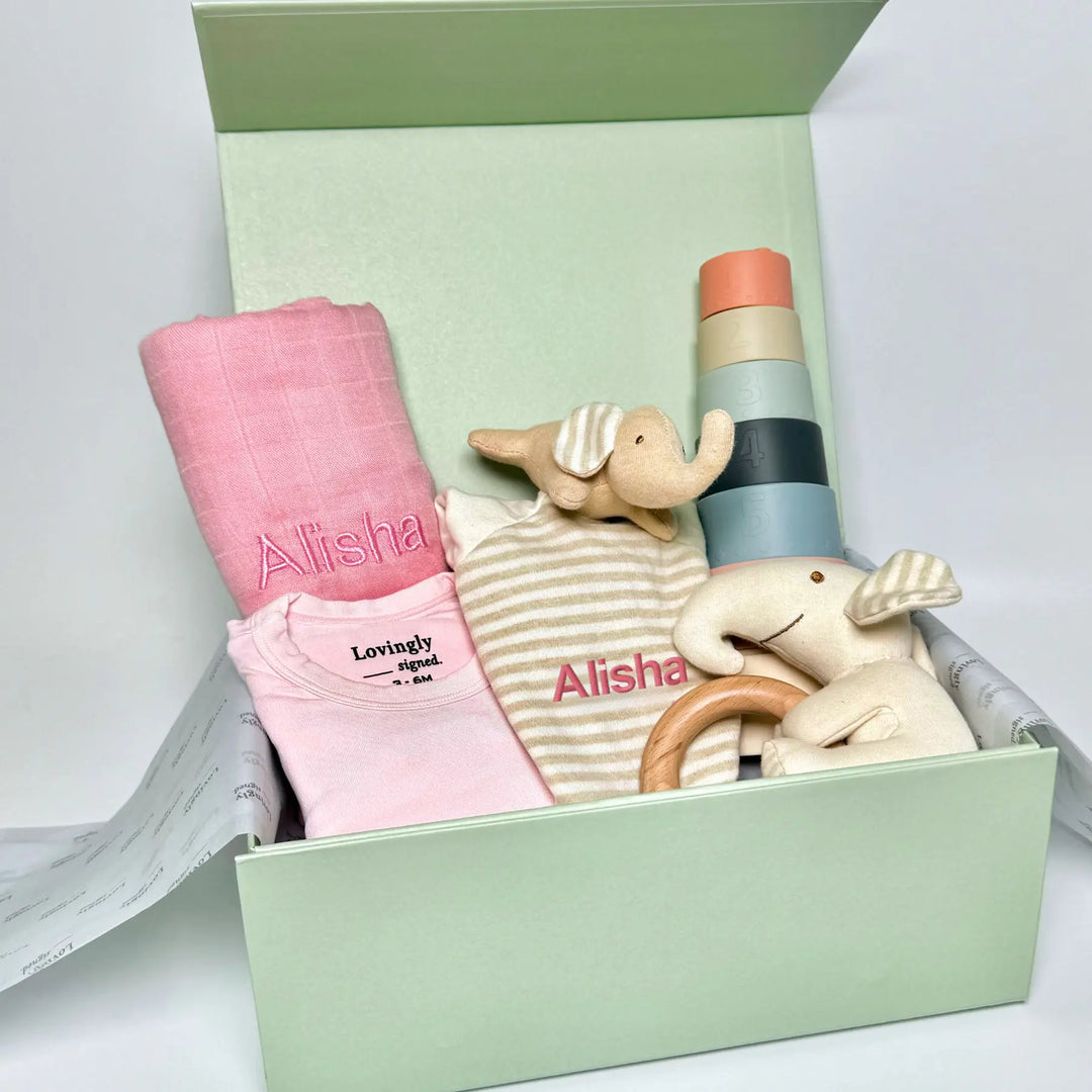Pink Baby gift set with clothes, toys, and a blanket in a lovingly signed gift box