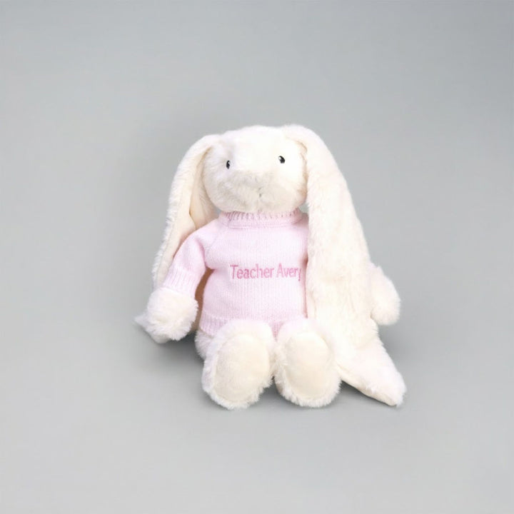 White plush bunny toy with pink sweater on a gray background