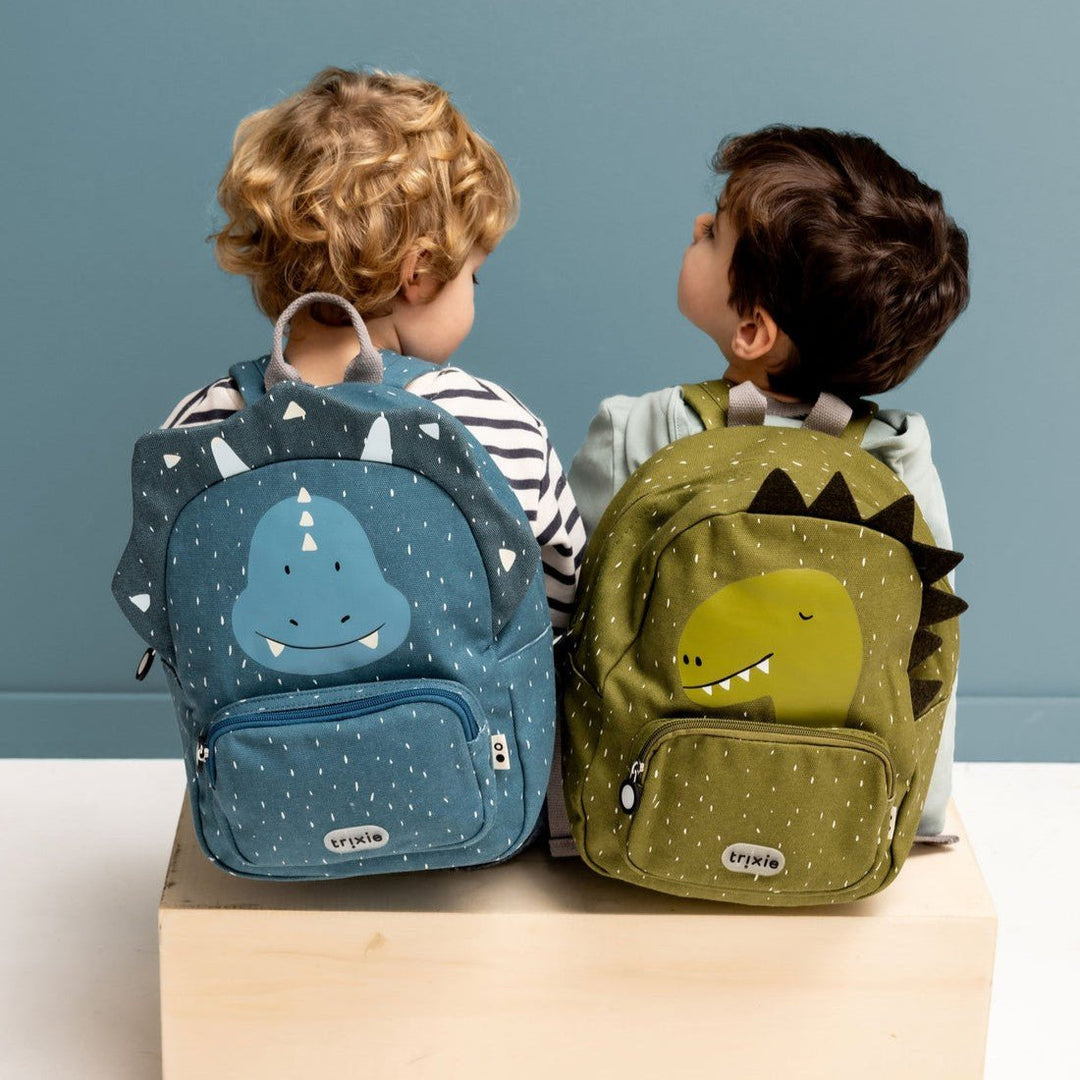 Two children with dinosaur-themed backpacks on a plain background