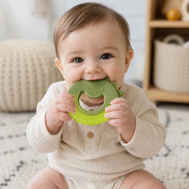 A baby wearing holding a Trixie Mr Dino Cooling Teether with a smiling face.
