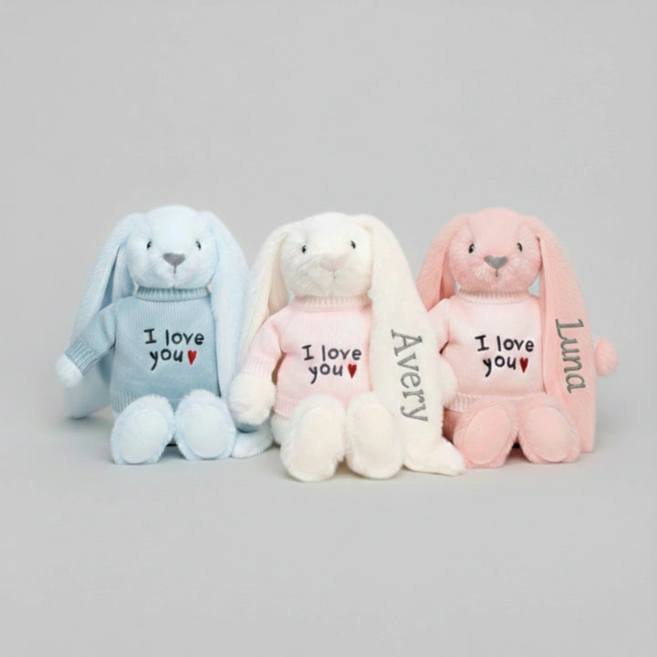 Three plush bunnies in blue, white, and pink with 'I love you' text on a gray background