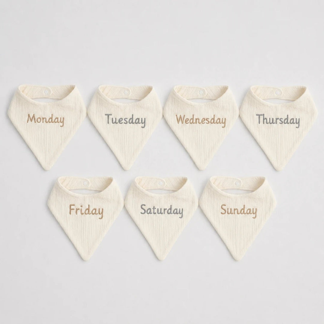 Set of seven cream-colored bibs with days of the week printed on them 
