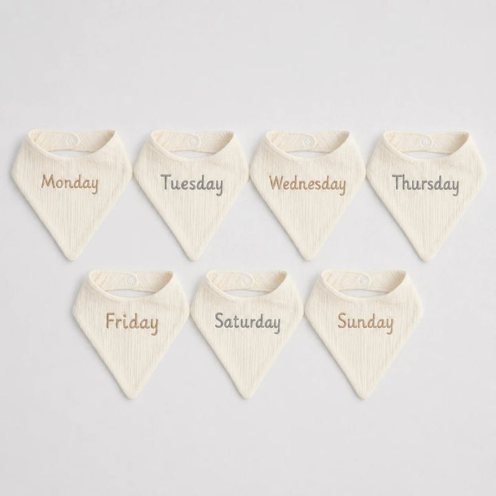 Set of seven cream-colored bibs with days of the week printed on them 