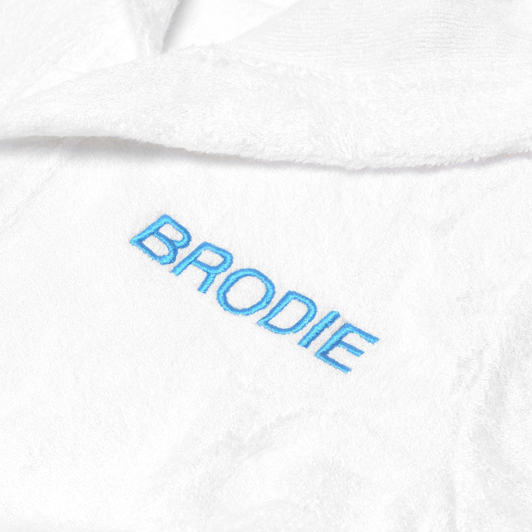 Baby in white bamboo robe with "BRODIE" customised in blue thread
