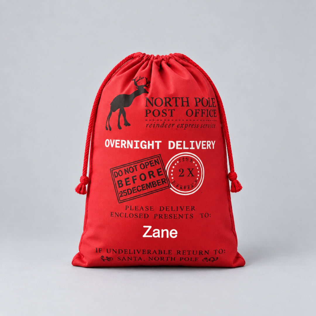 Personalised red Christmas drawstring sack featuring a black reindeer, North Pole Post Office design, festive delivery stamps and the name “Zane” in white.